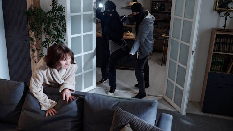 Woman escaping over couch while two masked burglars enter room